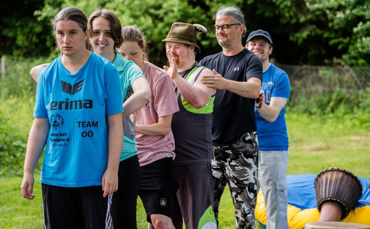 Gruppe von Erwachsenen blickt gemeinsam in die Kamera im Grünen bei einer Teamübung.