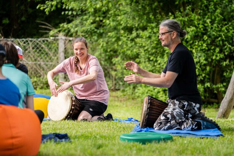 Mehrere Personen sitzen auf einer Wiese und spielen Trommeln.