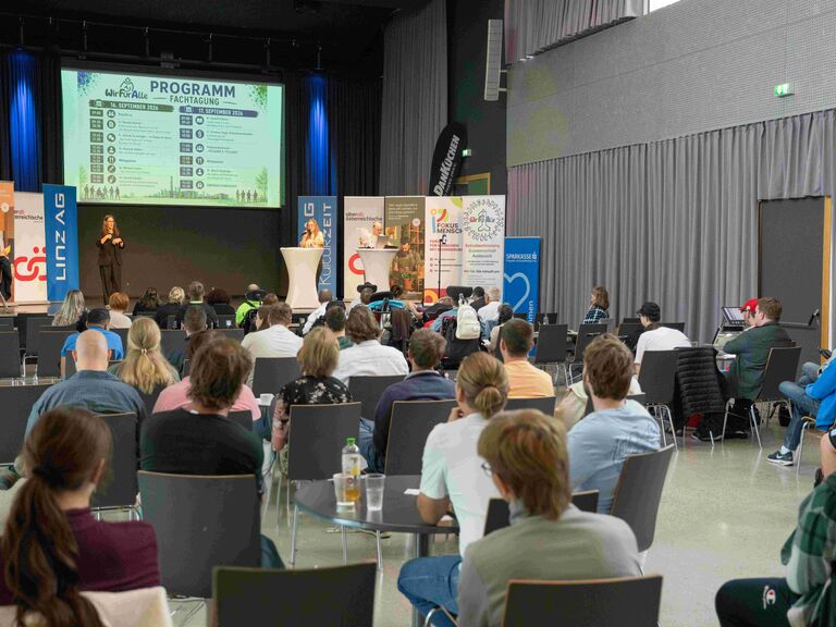 Blick übers Publikum hinweg fotografiert auf die Vortragsbühne