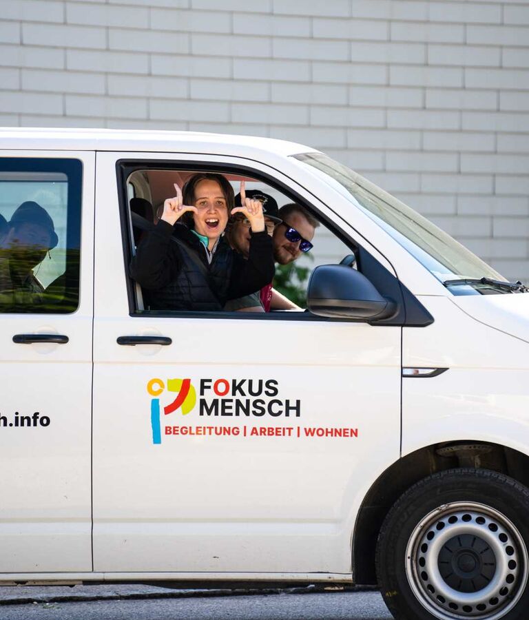 Zwei Personen sitzen in einem Fahrzeug mit FOKUS-MENSCH-Beschriftung und blicken aus dem offenen Fenster.