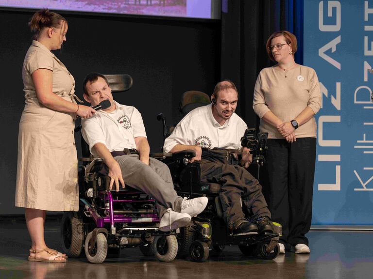 Podiumsgespräch, zwei Personen im Rollstuhl flankiert von Persönlicher Assistenz