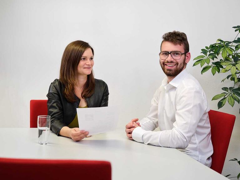 Zwei Personen sitzen sich an einem Tisch gegenüber und führen ein Gespräch mit Unterlagen – Bewerbungsgespräch oder berufliche Beratung.