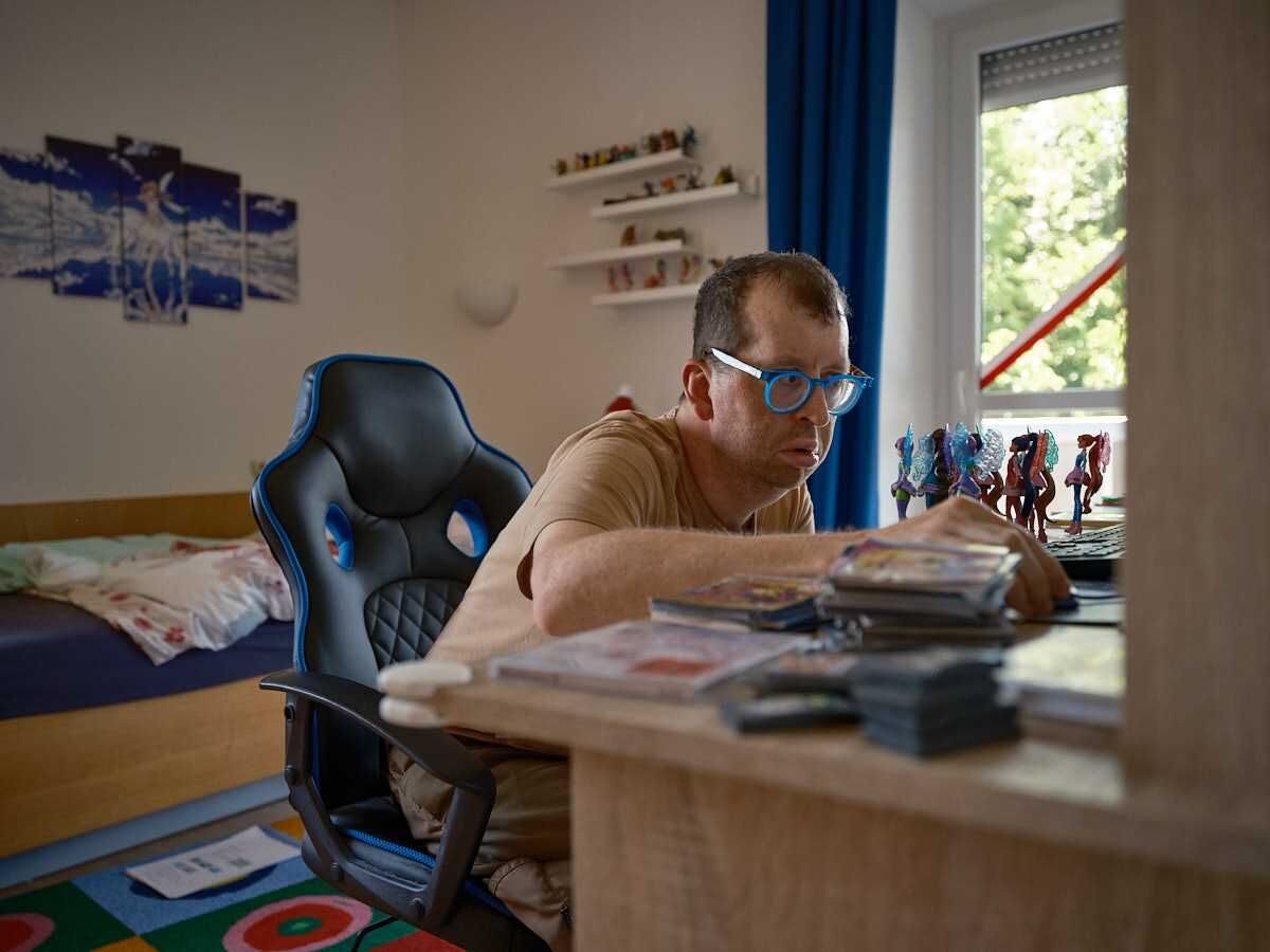 Ein Mann mit blauer Brille sitzt an einem Tisch und beschäftigt sich konzentriert mit Figuren und Karten – selbstbestimmte Freizeitgestaltung im eigenen Wohnraum.