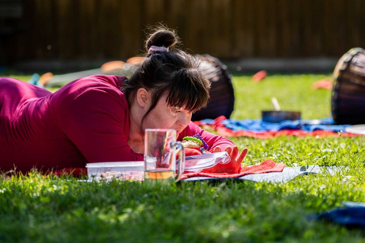 Frau liegt auf einer Wiese und betrachtet einen Gegenstand vor sich.