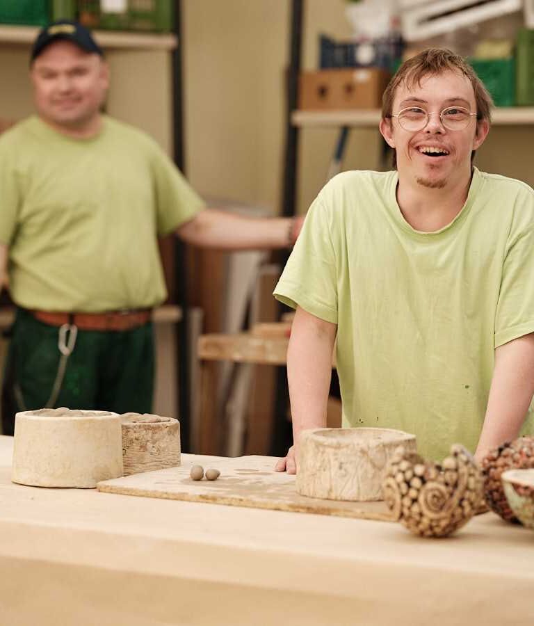 Zwei Männer stehen in einer Werkstatt, im Vordergrund sind mehrere Werkstücke zu sehen.