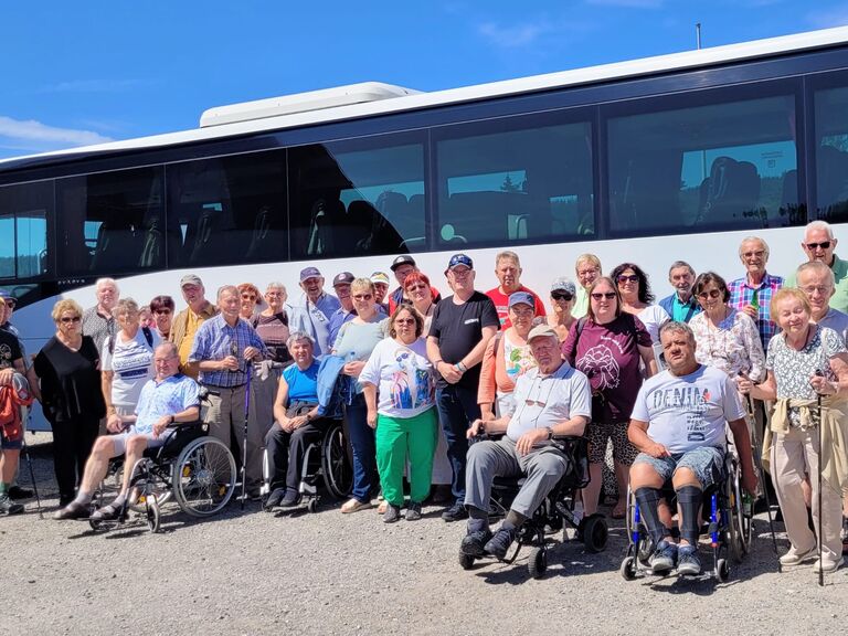 Gruppenfoto mit vielen Menschen stehend und im Rollstuhl sitzend vorm Reisebus