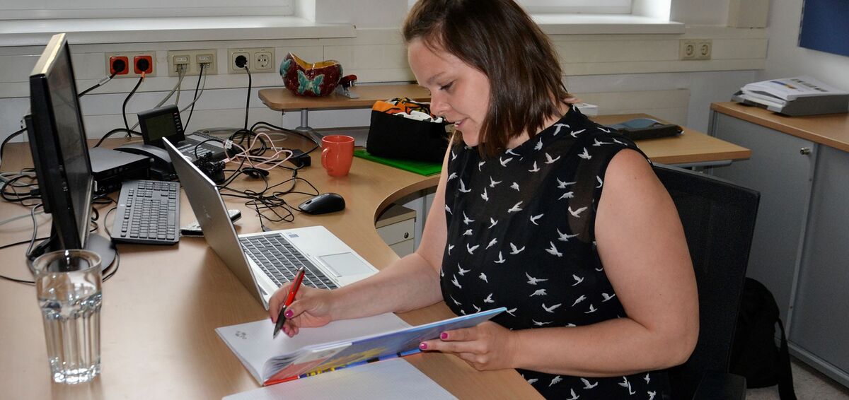 Eine Frau arbeitet an einem Schreibtisch im Büro und schreibt in ein Notizbuch.