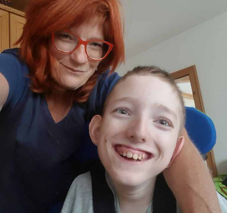 Eine Frau mit roten Haaren lächelt gemeinsam mit einem Jugendlichen in die Kamera – familiäre Begleitung und unterstützende Beratung im Alltag.