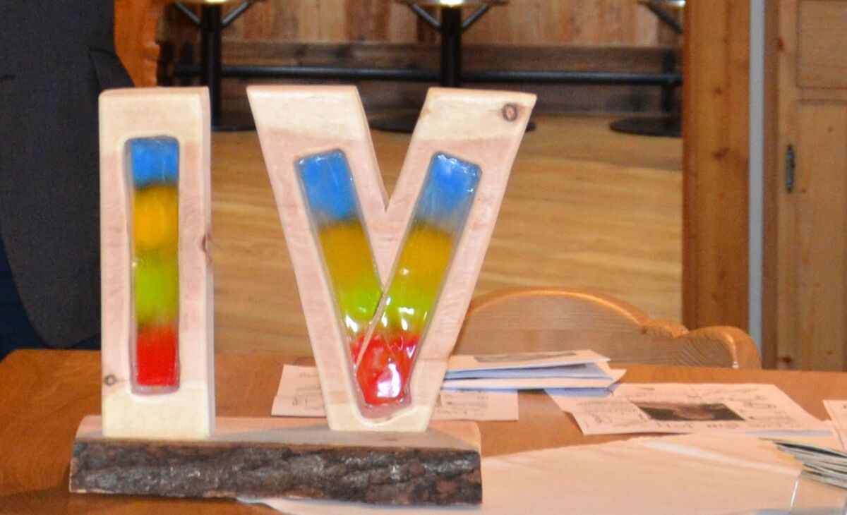 "I V" aus Holz auf einem Tisch mit Unterlagen als Symbolbild für Interessenvertretung