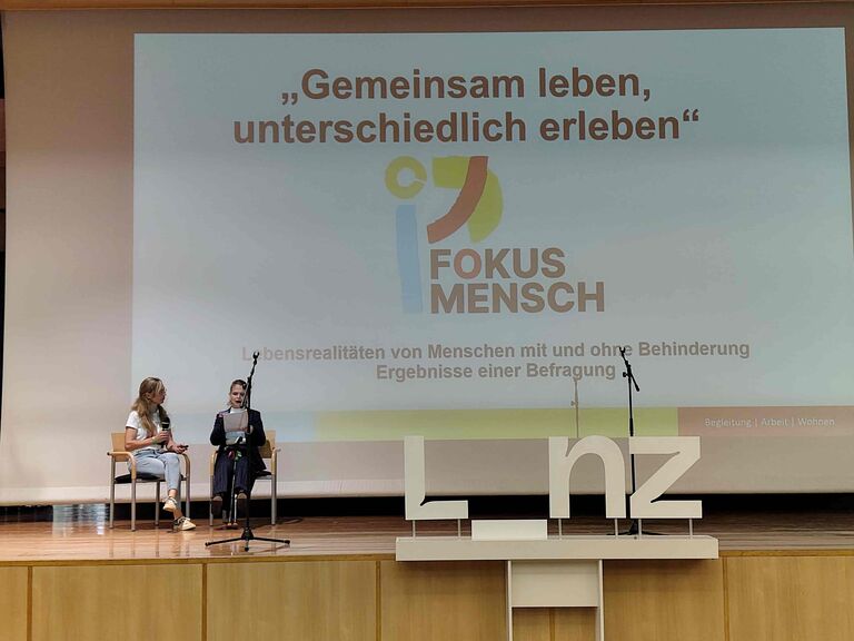 zwei Frauen sitzen auf der Bühne und halten einen Vortrag