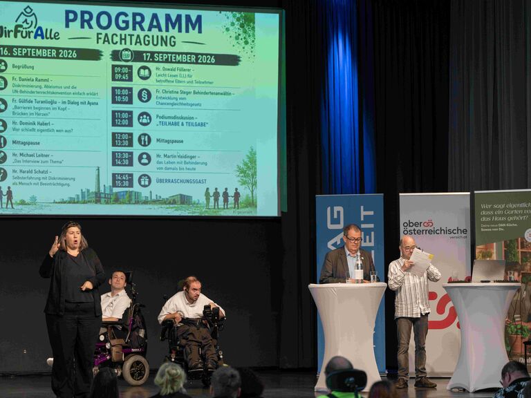 PodiumsVortrag mit mehreren Personen, Gebärdendolmetscherin, zwei Personen im Rollstuhl