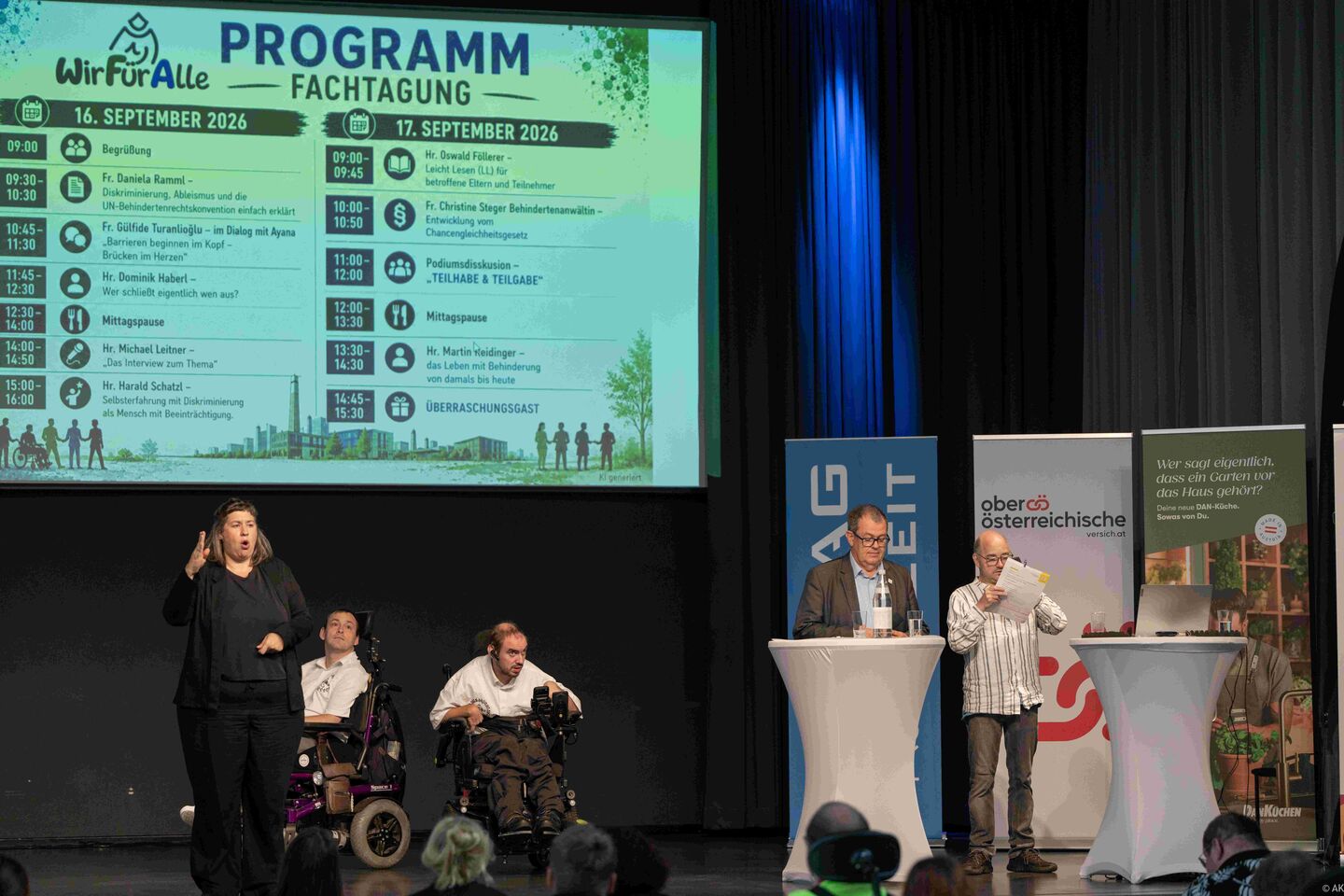 PodiumsVortrag mit mehreren Personen, Gebärdendolmetscherin, zwei Personen im Rollstuhl