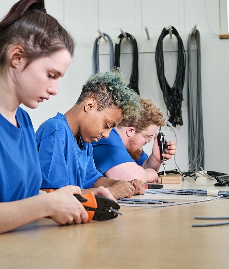 Mehrere Personen sitzen an einem Tisch und arbeiten konzentriert mit Werkzeugen.