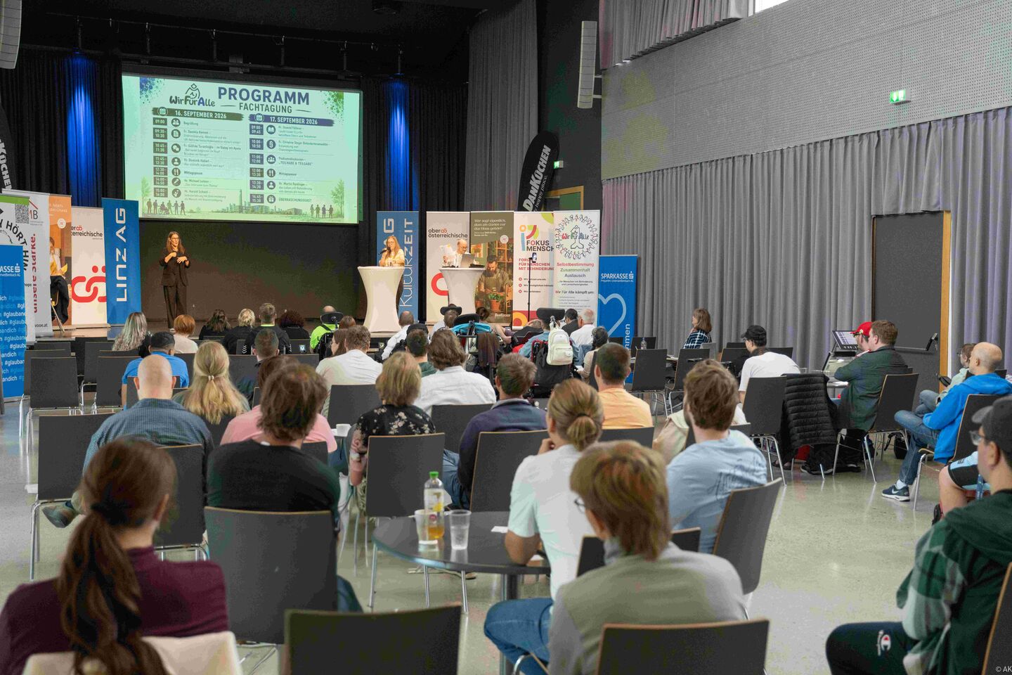 Blick übers Publikum hinweg fotografiert auf die Vortragsbühne