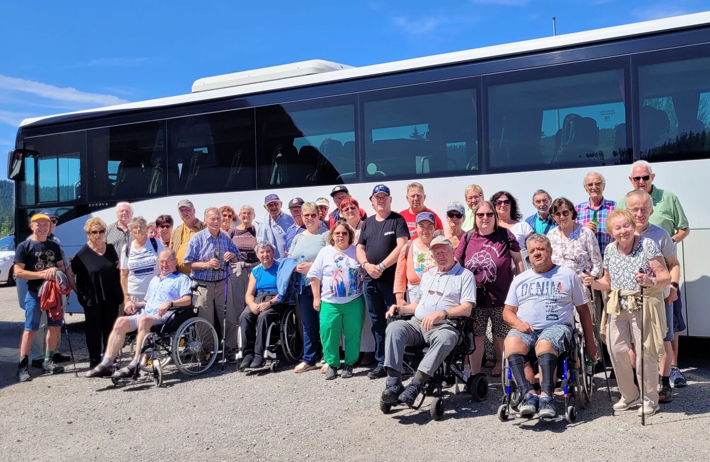 Gruppenfoto mit vielen Menschen stehend und im Rollstuhl sitzend vorm Reisebus