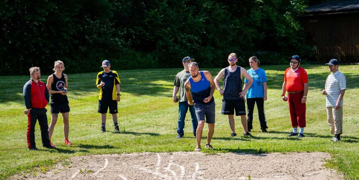 Mehrere Personen stehen auf einer Wiese und spielen ein Boccia oder ein ähnliches Spiel.