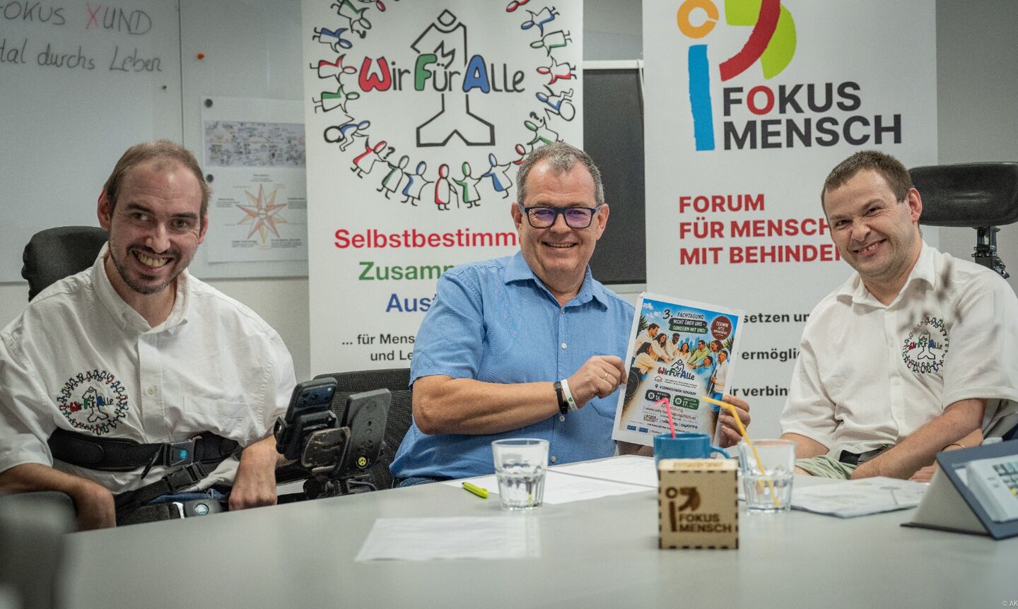 drei Männer am Besprechungstisch, einer hält 