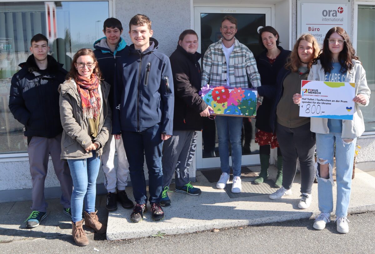 Gruppe junger Menschen übergibt einen symbolischen Spende-Scheck