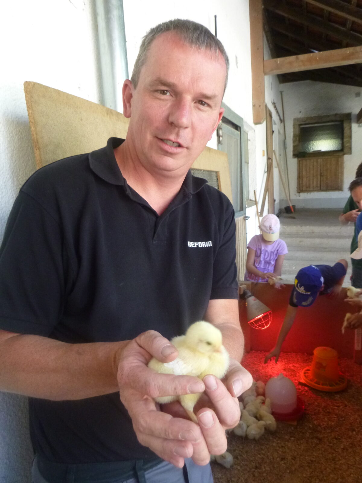 Ein Mann hält ein Küken in die Kamera.
