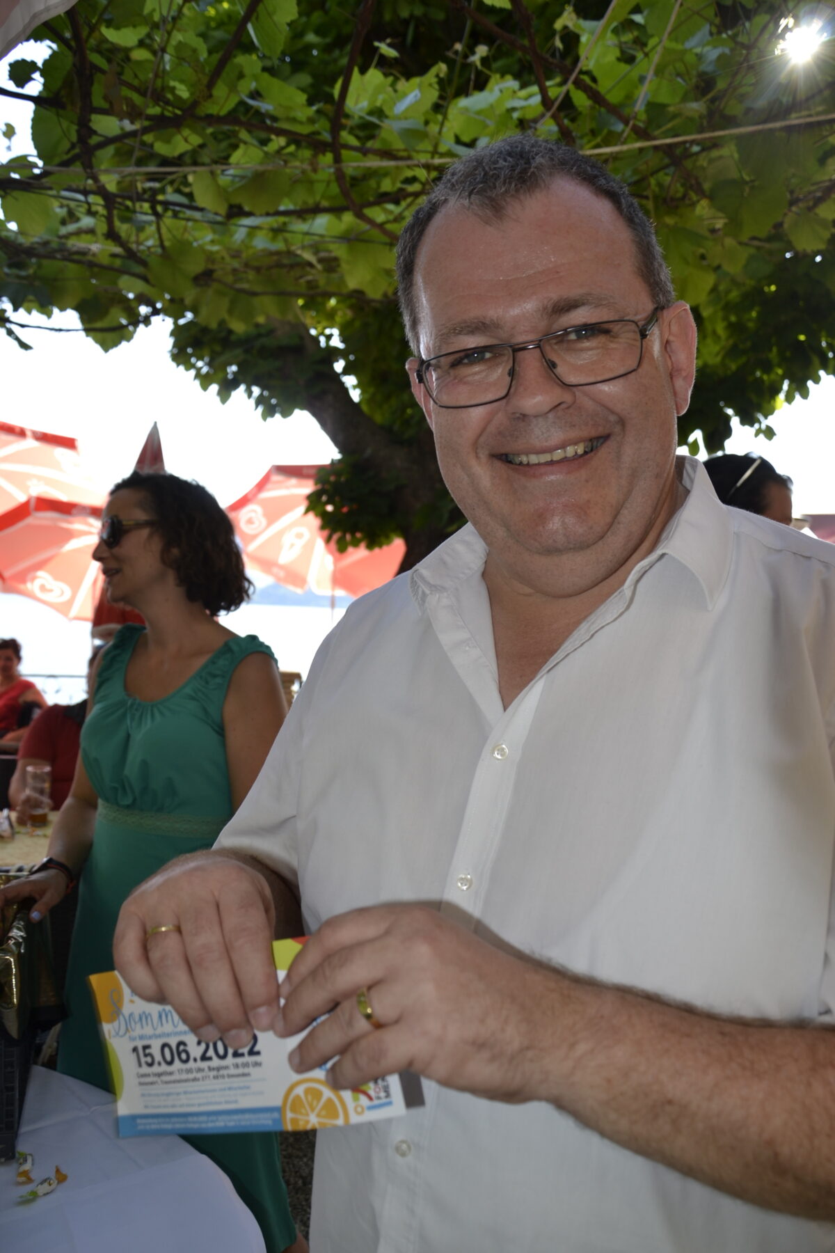 Mann lacht in die Kamera, hält Einladung zum Sommerfest