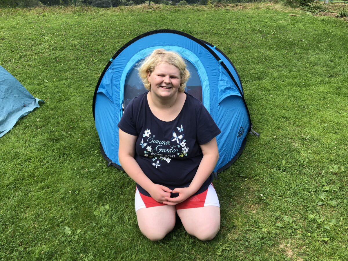 junge Frau sitzt vor einem ein-Personen-Zelt und lächelt in die Kamera