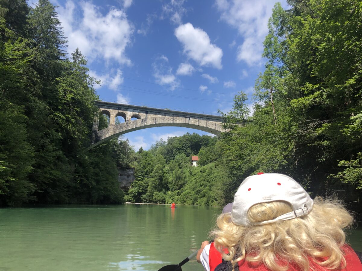 junge Frau im Paddelboot von hinten, blickt auf Wasser und Brücke