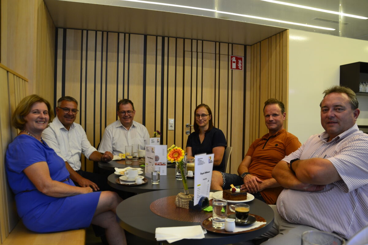 eine Gruppe von Menschen sitzt rund um einen Kaffeetisch und lächelt in die Kamera