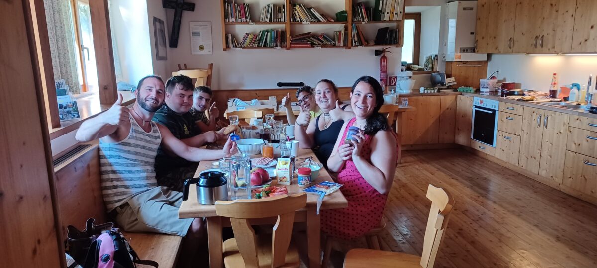 Gruppe sitzt rund um den Frühstückstisch und lacht in die Kamera