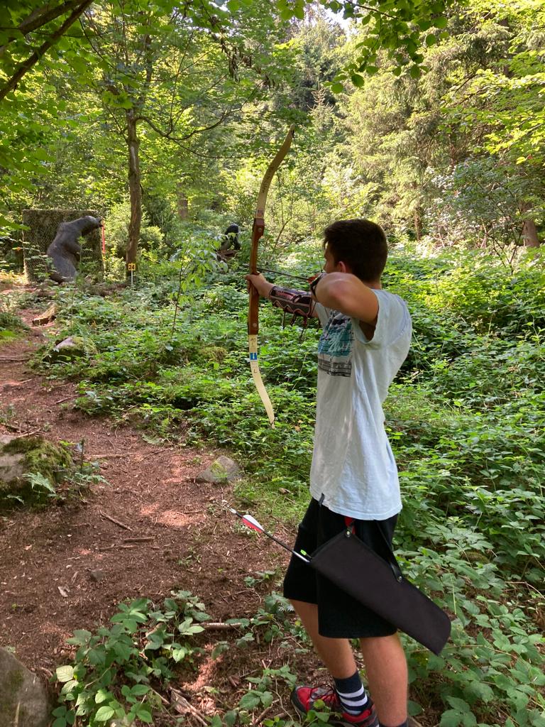 junger Mann als Bogenschütze, zielt auf einen Holz-Bären