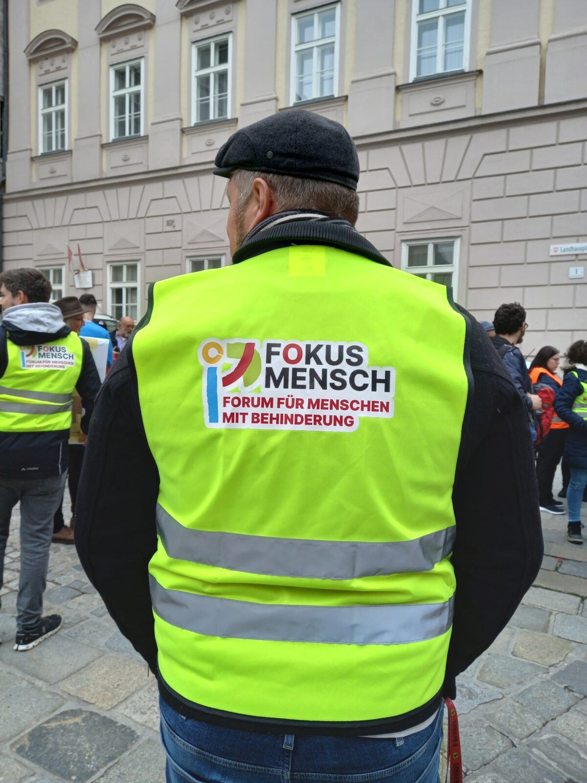 Mann von hinten mit Warnweste, auf der das Fokus Mensch-Logo ist