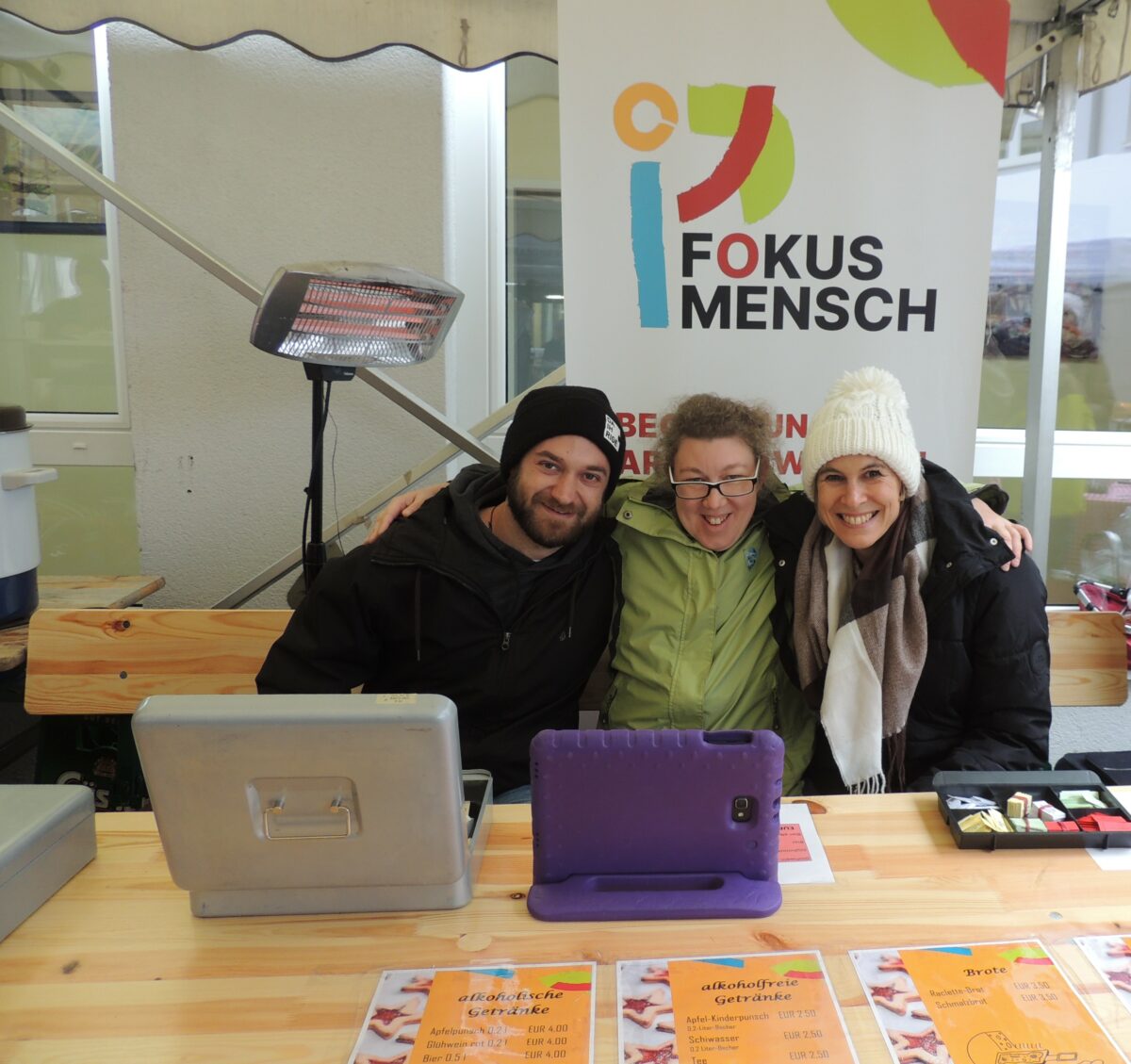 drei Menschen sitzen vor der Kassa-Box