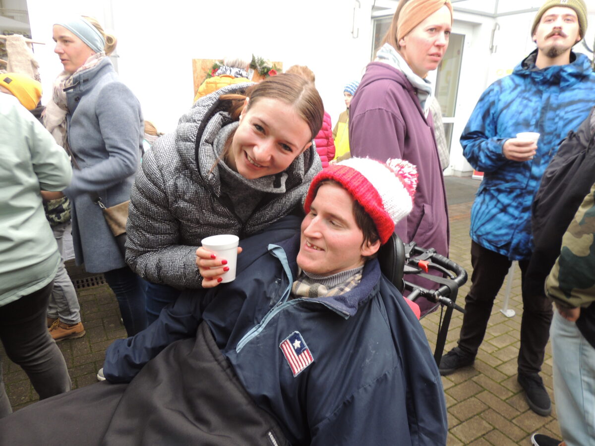 zwei Besucherinnen trinken Punsch, eine Frau sitzt im Rollstuhl 