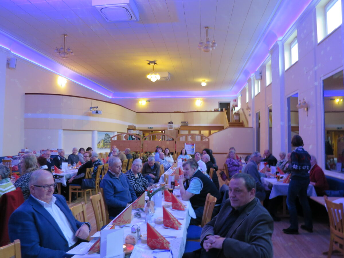 große Gruppe von Menschen sitzt an langen Tischen in einem Gasthaus