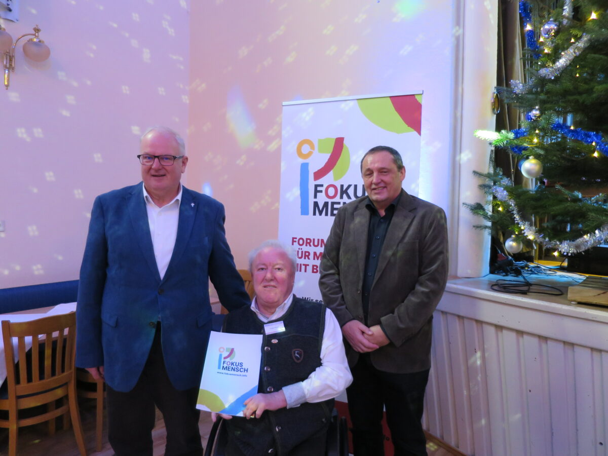 drei alte ältere Herrn lächeln in die Kamera, einer sitzt und hält eine Urkunde