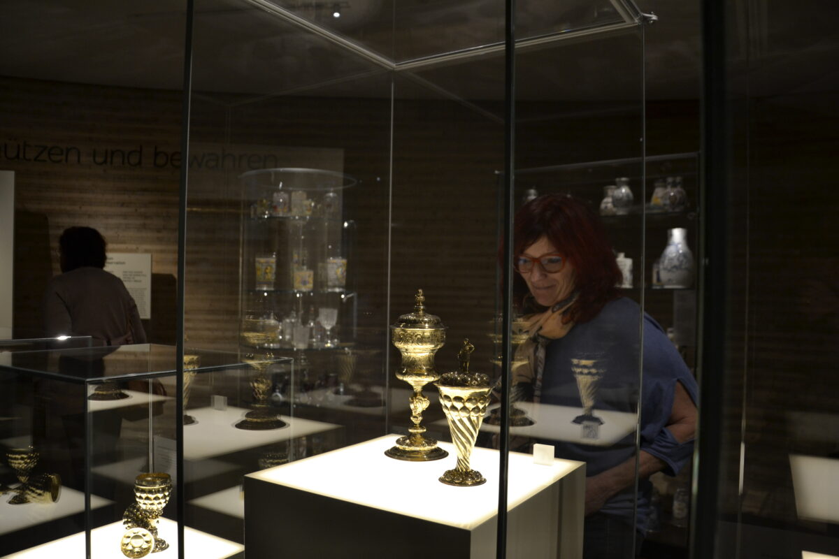 Frau betrachtet durch Vitrine einen goldenen Zunftbecher