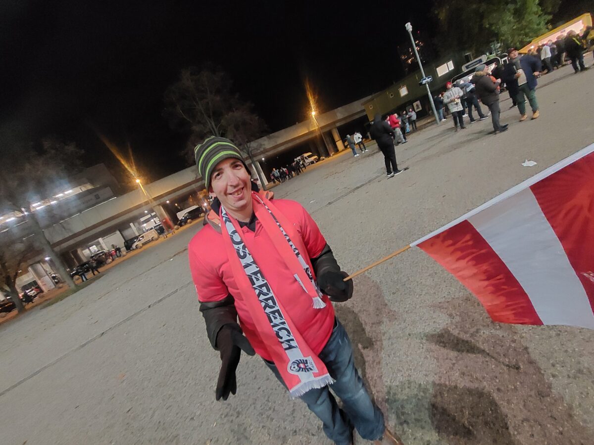 junger Mann mit Österreich-Fanschal schwenkt Österreich-Fahne