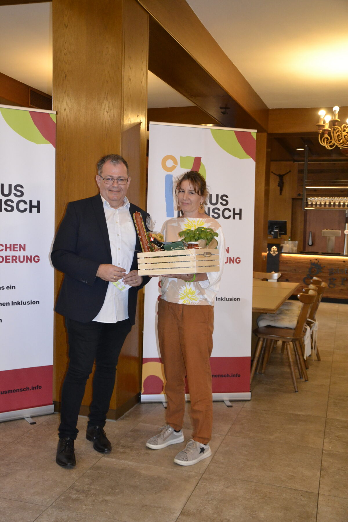 Ehrung langjähriger Mitarbeiterinnen und Mitarbeiter - eine Frau mit Geschenkkorb, daneben steht Mann