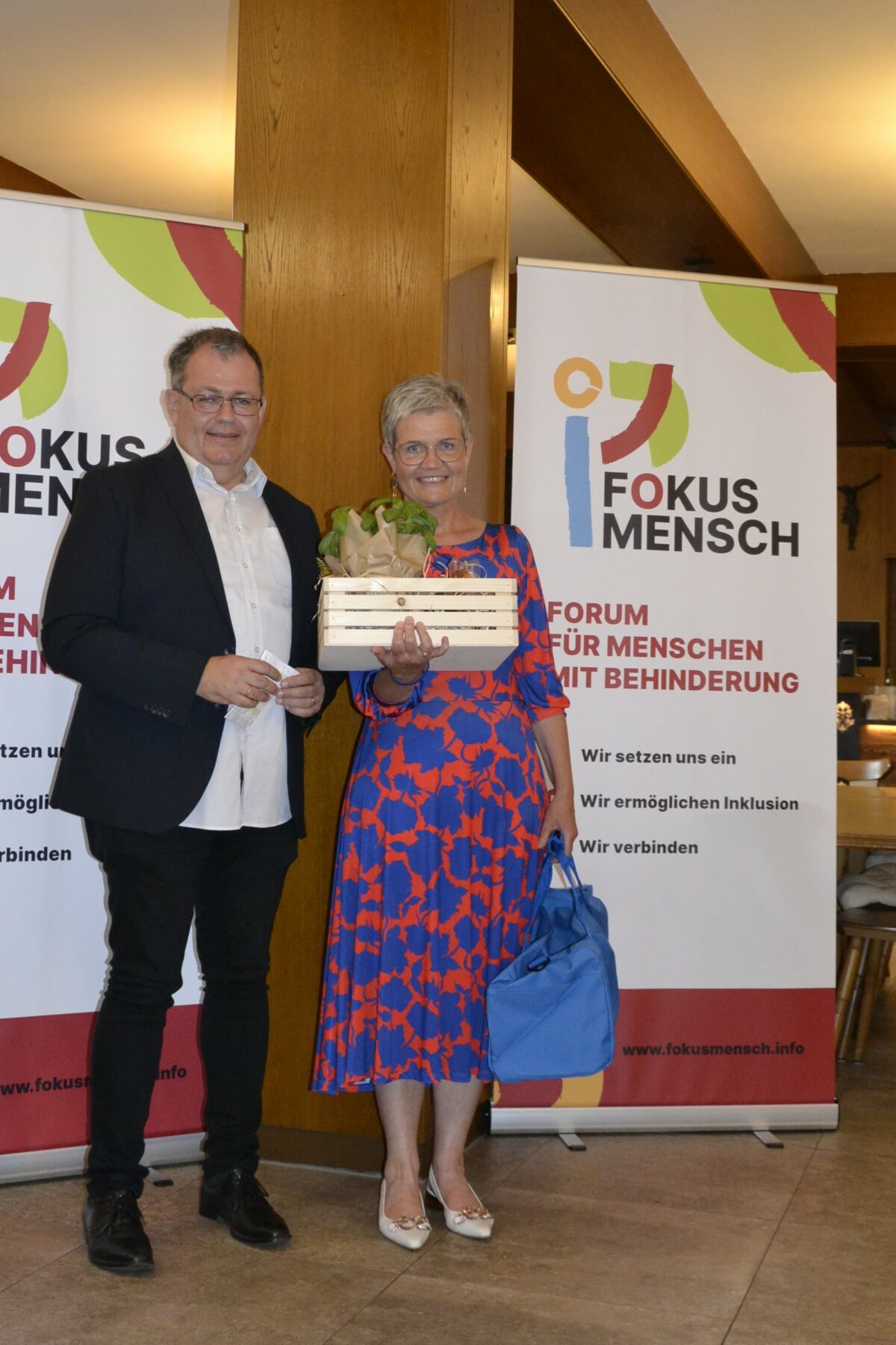 Ehrung langjähriger Mitarbeiterinnen und Mitarbeiter - eine Frau mit Geschenkkorb, daneben steht Mann