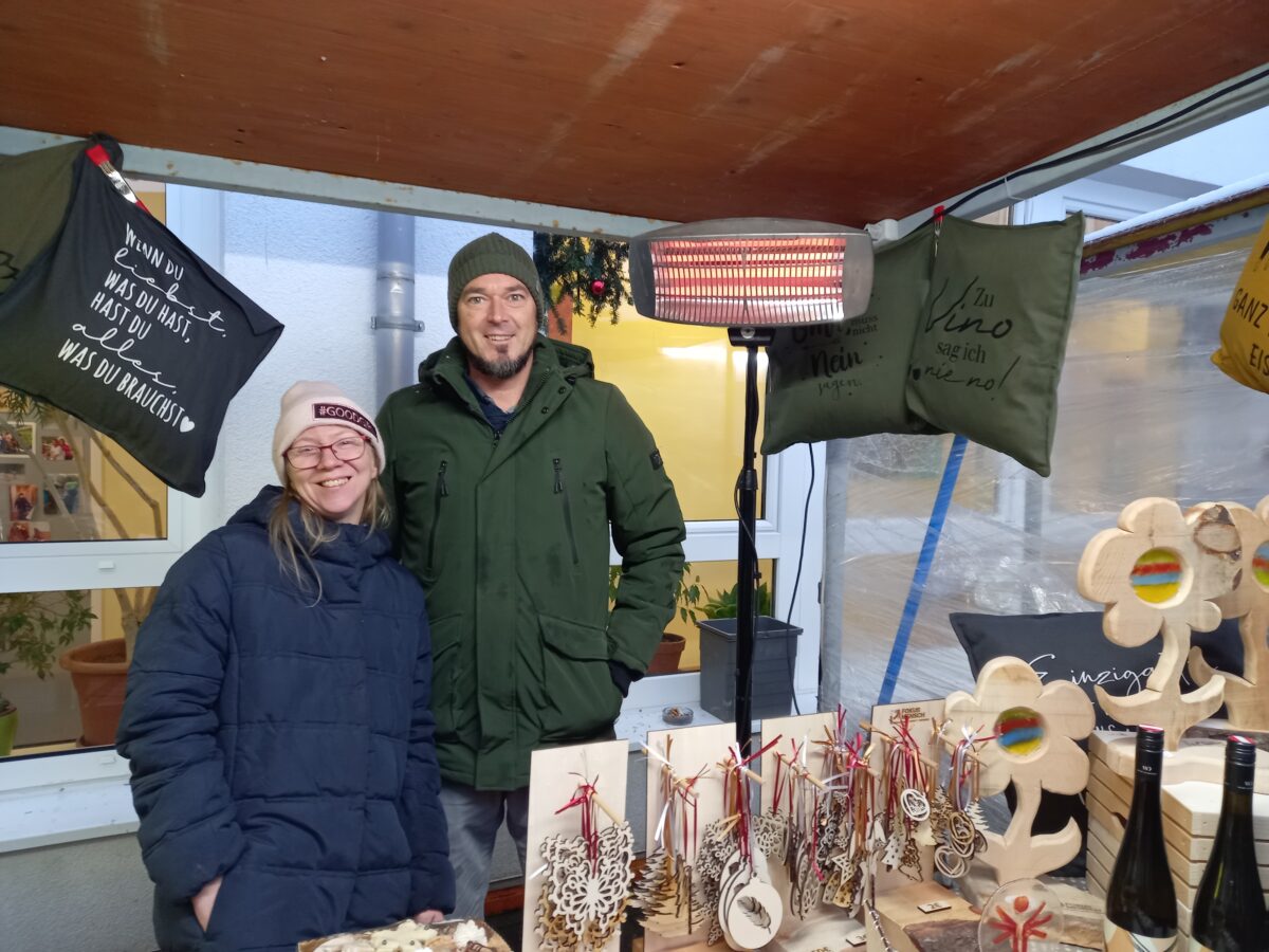 zwei Menschen stehen hinter einem Verkaufsstand, lachen in die Kamera