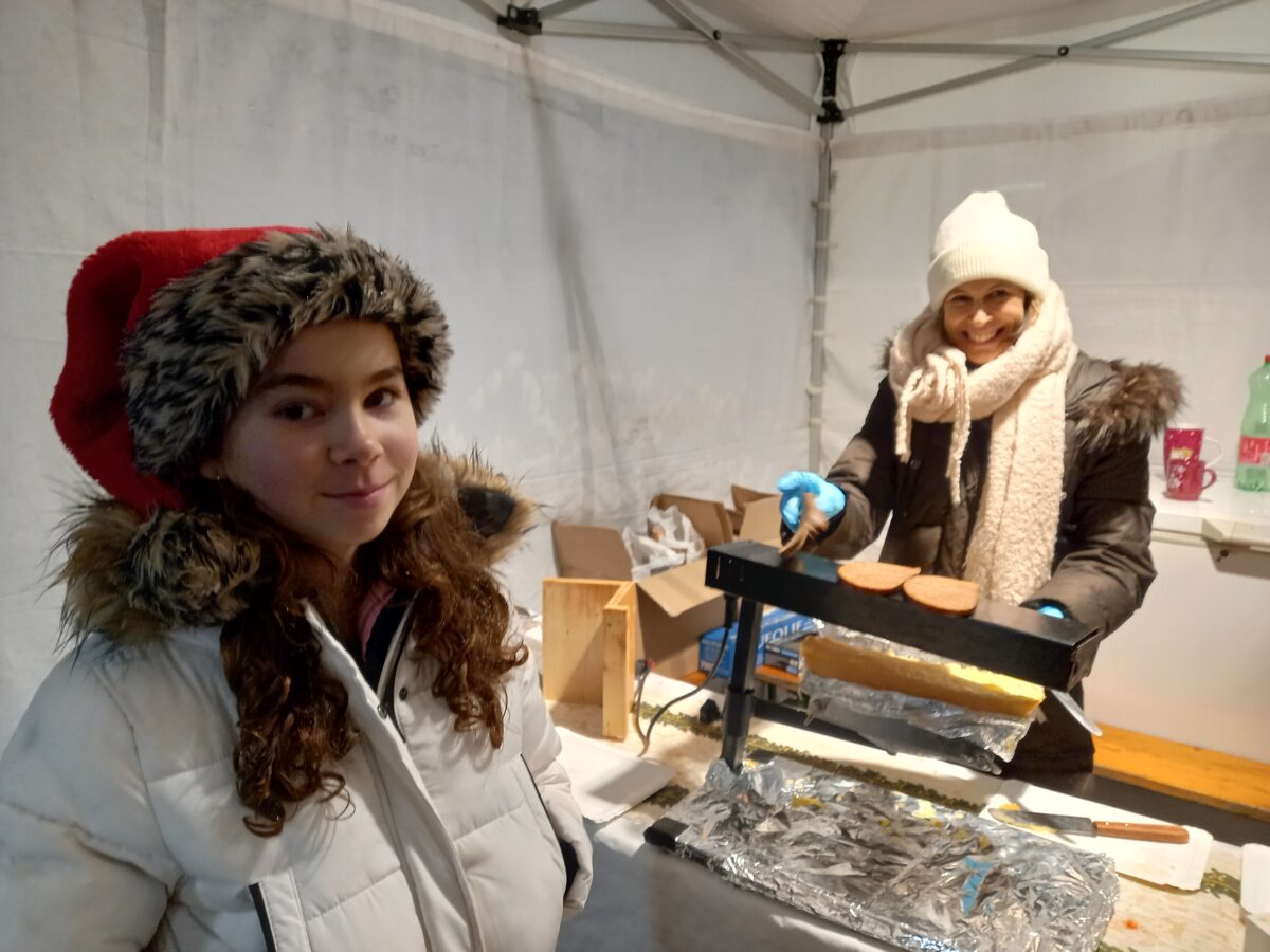 Frau macht Raclette-Brot, Mädchen steht da und lächelt