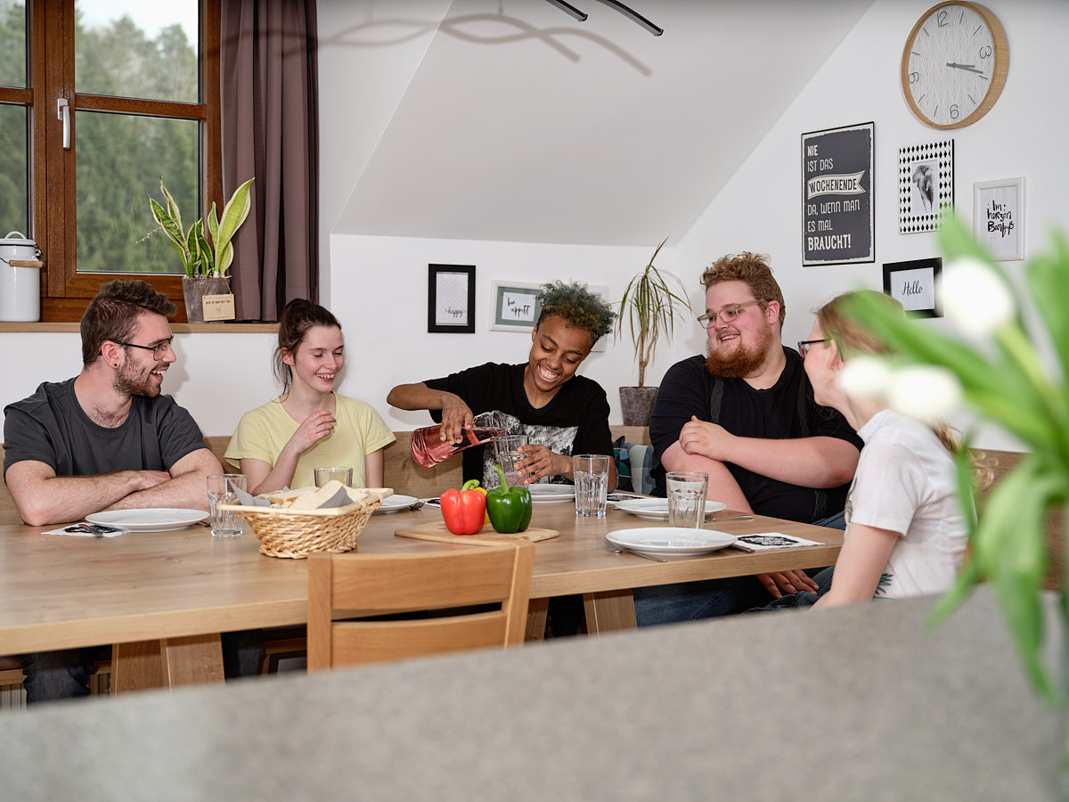 fünf junge Menschen sitzen bei einem gedeckten Tisch und lachen