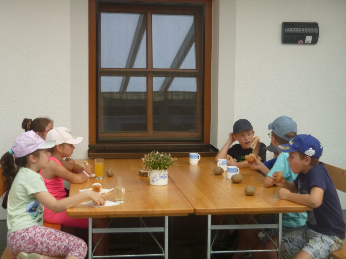 Kinder sitzen bei Tisch und jausnen

