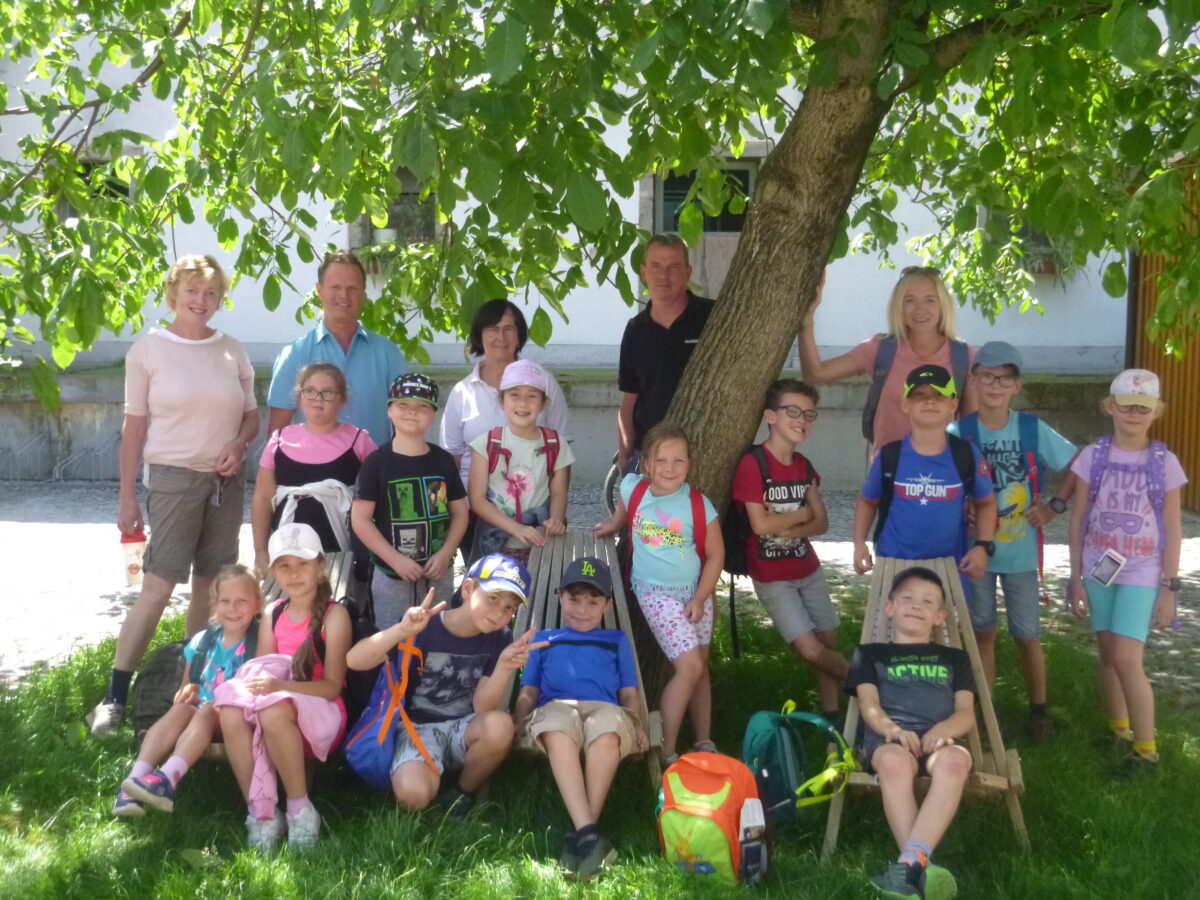 Gruppenfoto mit Schülerinnen und Schülern und einigen Erwachsenen, die im Schatten eines Baumes stehen und teilweise sitzen