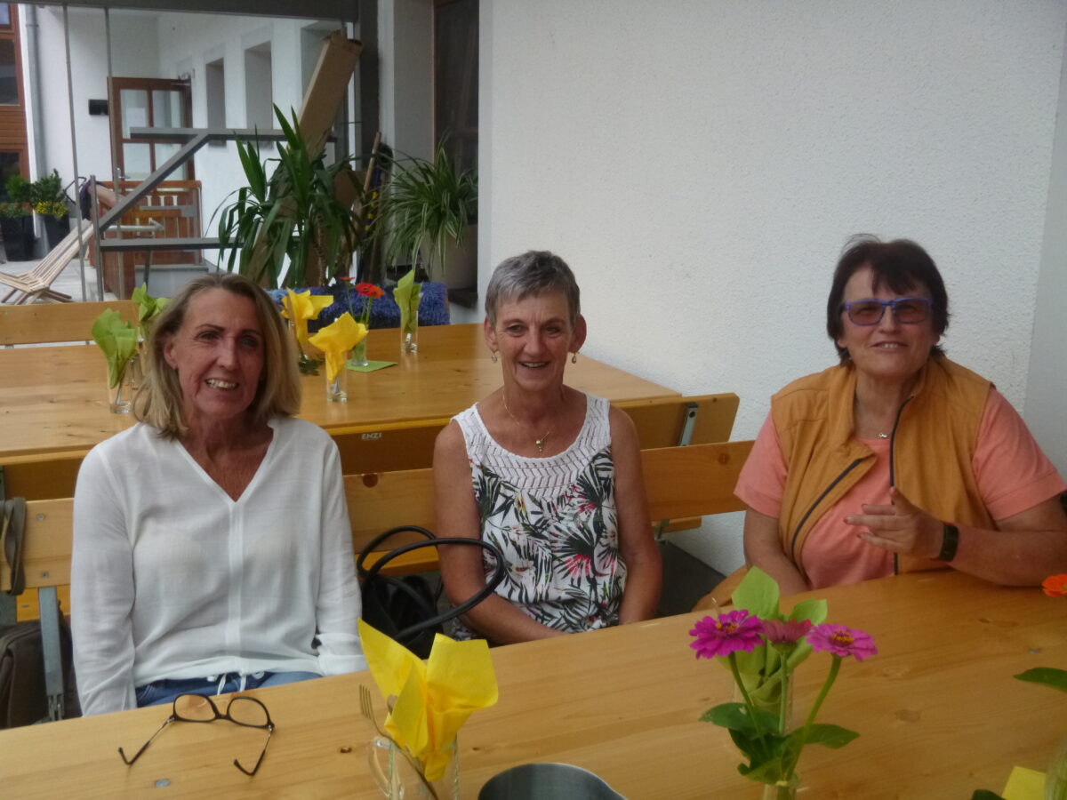 drei ältere Damen sitzen bei Tisch und lachen in die Kamera