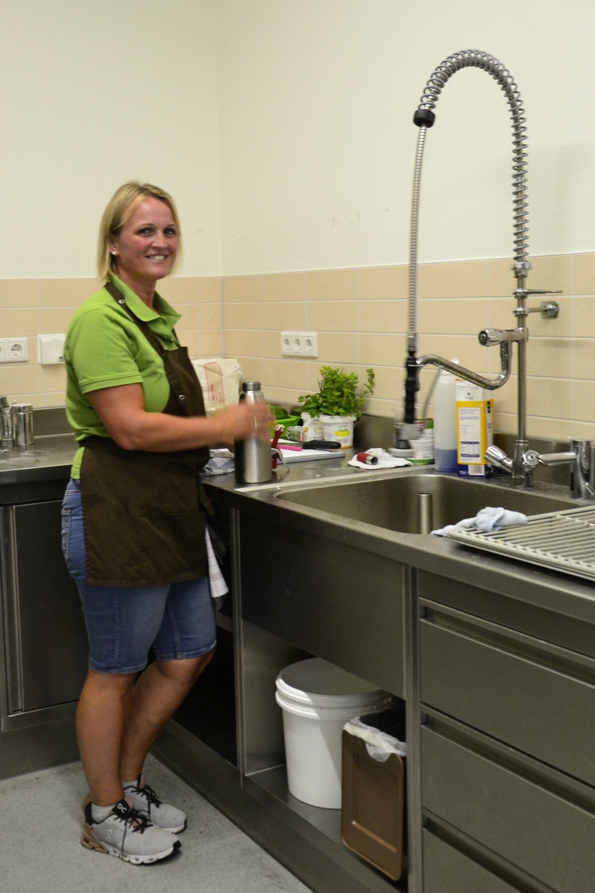 eine Frau steht an der Abwasch in der Küche und lächelt in die Kamera