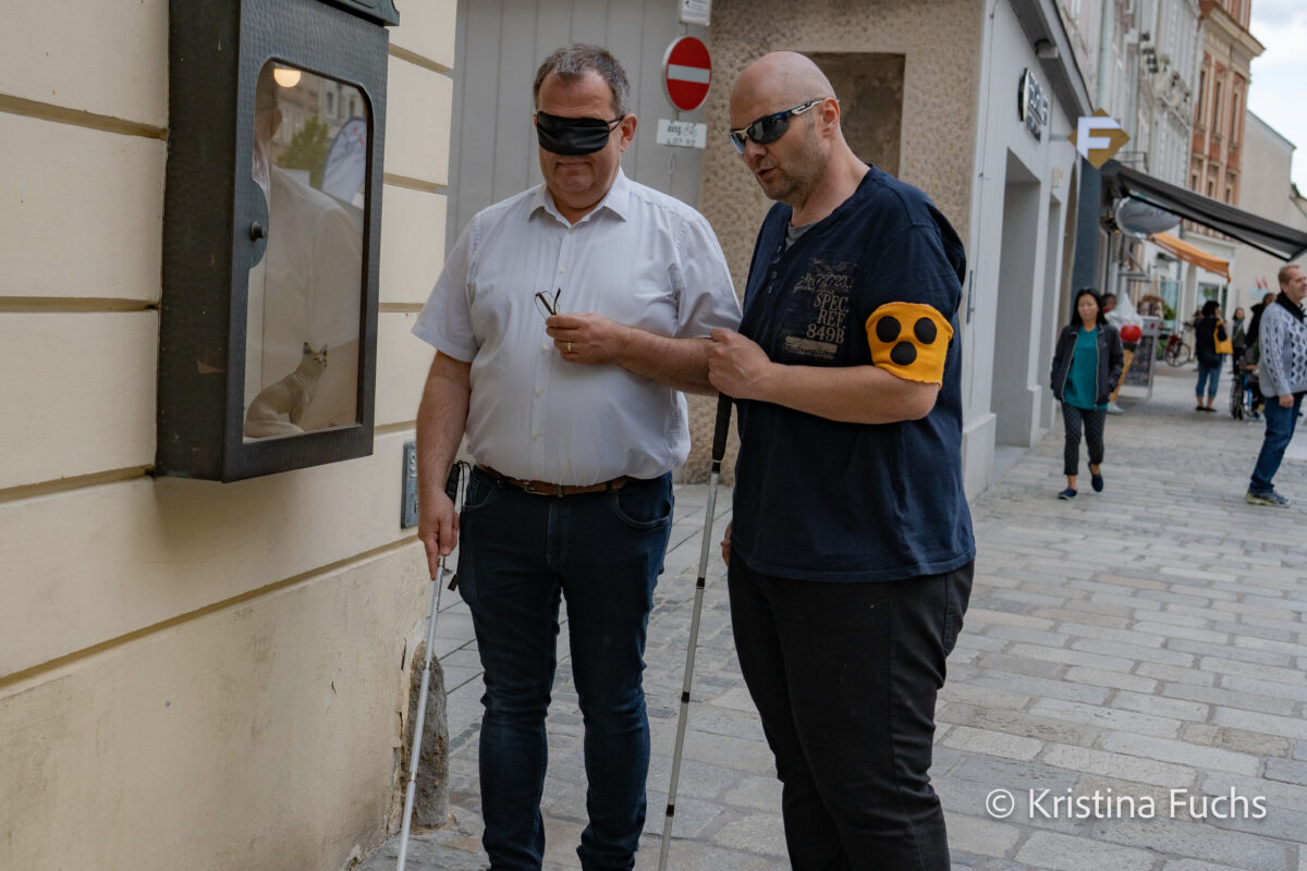Ein blinder Mann und ein Mann mit Augenbinde erkunden die Stadt