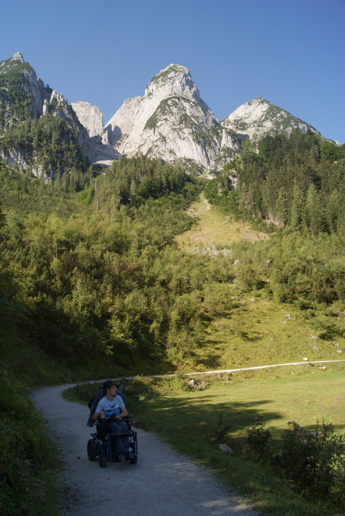 Mann im Rollstuhl unterwegs auf Wanderweg, im Hintergrund ist Gebirge