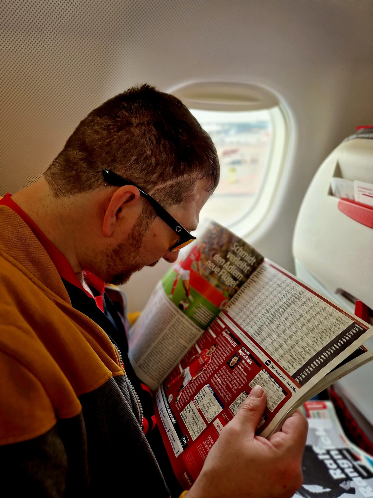 Mann liest Fußball-Zeitschrift, sitzt im Flugzeug