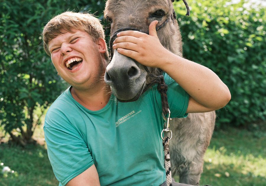 junger Mann lacht, umarmt einen Esel