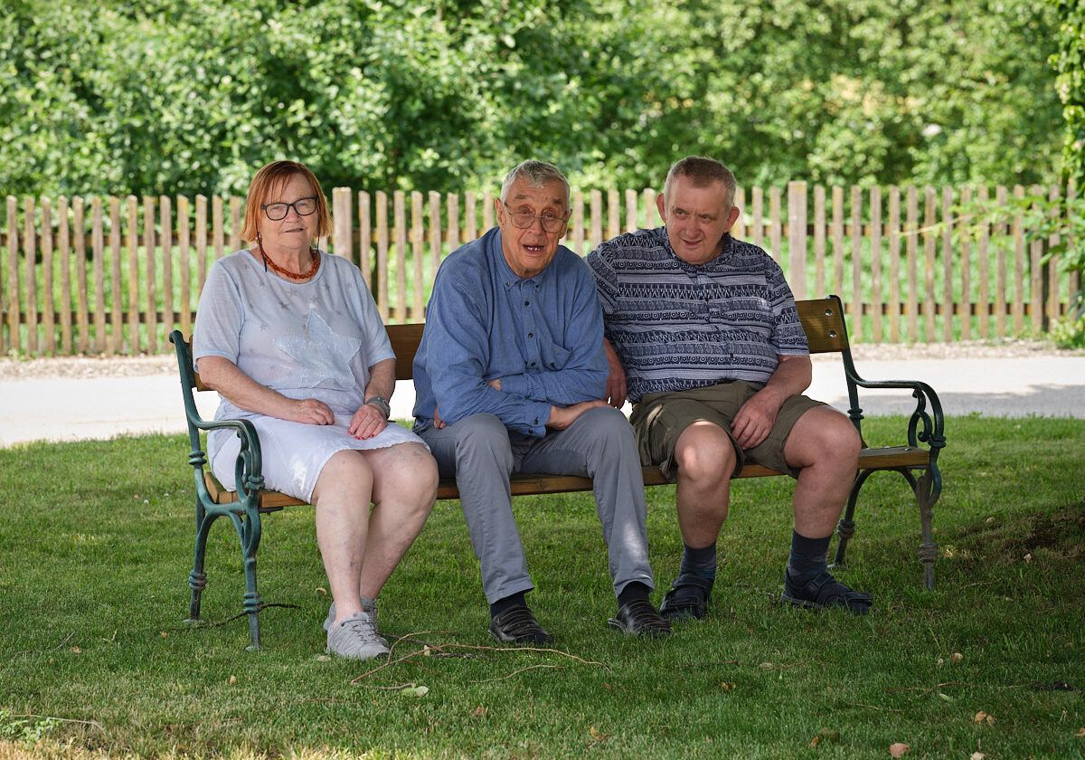 drei ältere Menschen sitzen auf einer Parkbank im Schatten
